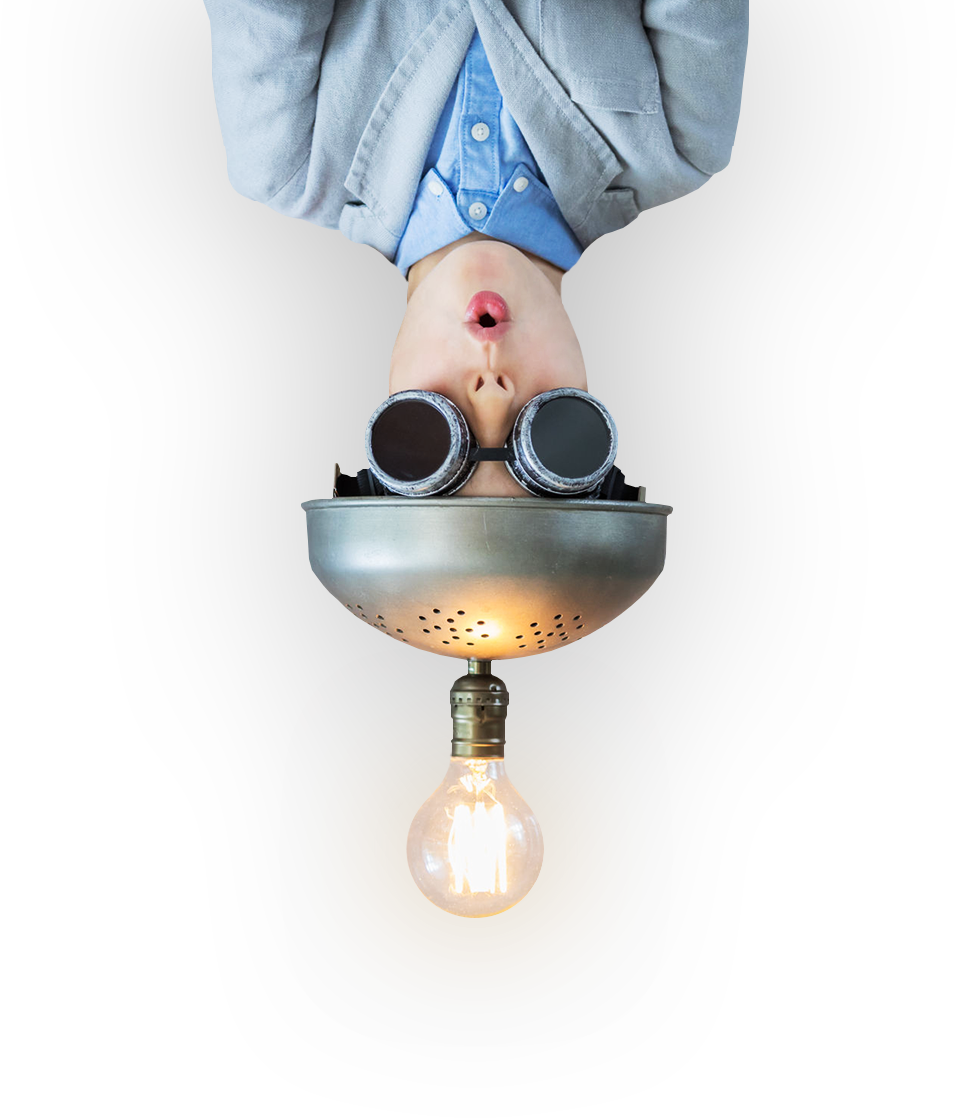 A child hanging upside down wearing a colander as a thinking cap and welding goggles, with a lit filament bulb below.