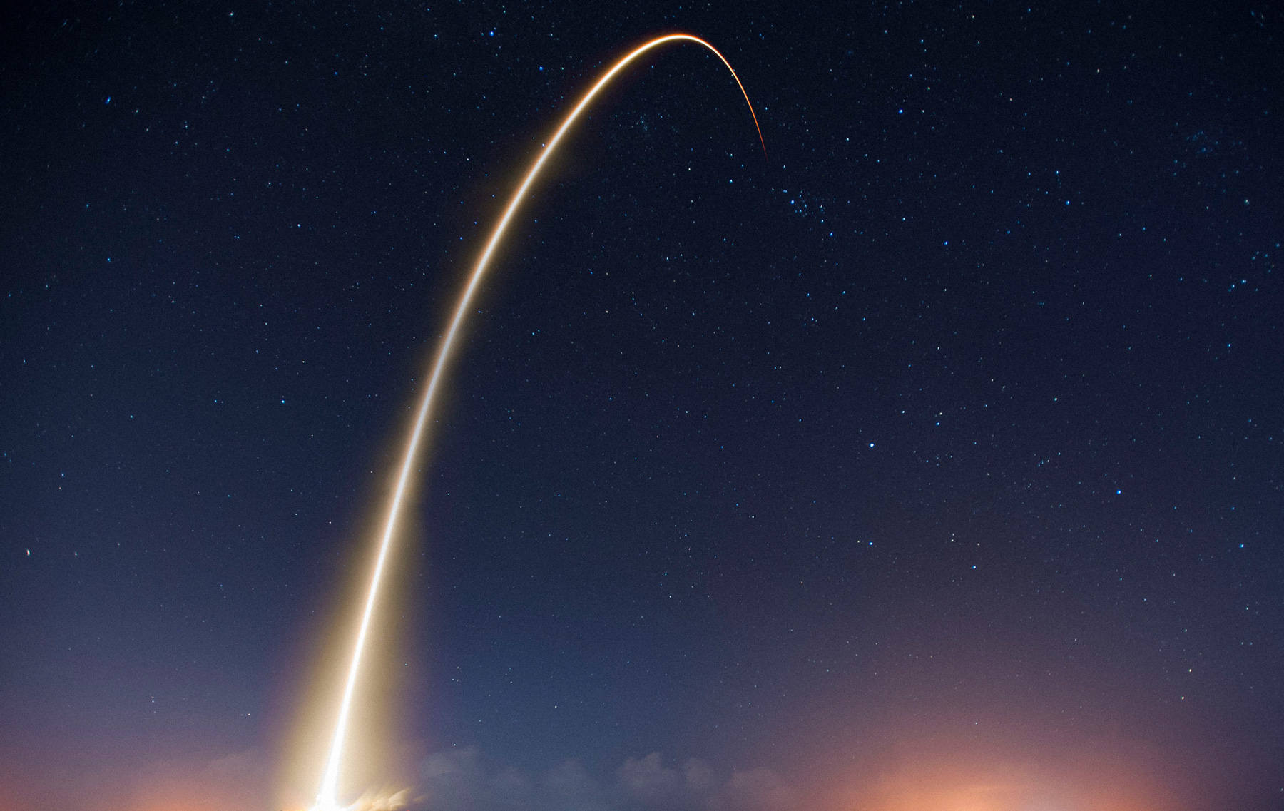 A long-exposure rocket launch arc against a twilight sky.